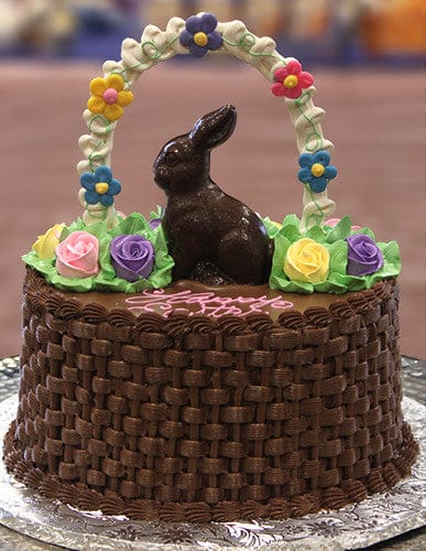 The EA-025 is a chocolate cake featuring basket-weave frosting, a chocolate bunny, colorful icing flowers, green leaves, and an arch crafted from decorative icing flowers.