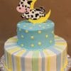 BB-002: A two-tier cake featuring pastel stripes on the bottom and a blue top tier with yellow stars, topped with a cartoon cow leaping over a yellow crescent moon.