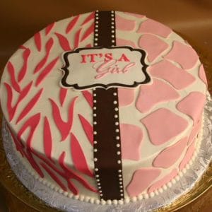 BB-035 is a round cake featuring pink and white animal print patterns, a brown vertical stripe with white dots, and a topper that reads “IT’S A Girl” in pink and red letters.