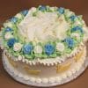 BB-008 is a round cake adorned with white and blue rose-shaped icing, green leaves, white chocolate shavings on top, yellow duck shapes on the sides, and piped white icing along the base and edges.