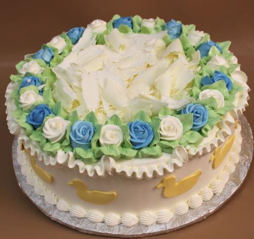 BB-008 is a round cake adorned with white and blue rose-shaped icing, green leaves, white chocolate shavings on top, yellow duck shapes on the sides, and piped white icing along the base and edges.