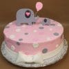 Product BB-043: A round pink cake with white, pink, and gray polka dots, topped with two fondant elephants (large and small) holding a pink balloon, and finished with a white fondant bow at the base.