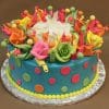 The BD-057 cake features blue frosting, vibrant pink, orange, green, and yellow fondant flowers and dots, finished with a yellow icing border at the base and presented on a foil-covered board.