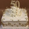 The BD-063 cake features a square white base with gold music notes, white roses, elegant swirls, and a large gold "50" topper. "Happy Birthday Ivano" is piped in gold icing. The cake is set on a patterned base for an elegant finish.