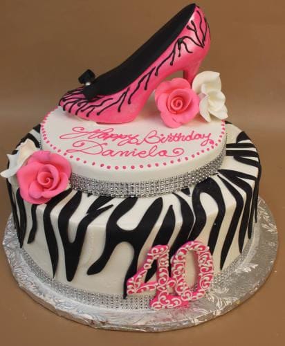 The BD-034 Zebra Shoe is a two-tier zebra-striped cake with pink roses, white flowers, a pink high heel on top, the number 40, and "Happy Birthday Daniela" in pink icing.