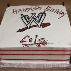 The ST-010 Wrestling cake is rectangular and decorated as a wrestling ring with red ropes, black corner posts, the WWE logo, and "Happy 5th Birthday Cole" written in black and red icing.