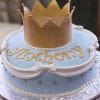 CB-016A is a round cake with light blue fondant, white bows, gold accents, and "Anthony" in gold letters. A large gold fondant crown decorates the top.
