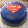 The CB-006E is a round blue cake with a red and yellow Superman logo on top, “Happy Birthday” and “Dave” in red icing, and a yellow bead border around the base.