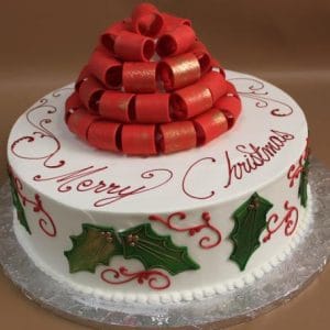 The CH-042 is a round white cake with "Merry Christmas" in red icing, green holly leaves, and a red ribbon bow topper, presented on a silver cake board.