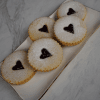 Five CE-000B Raspberry Linzer cookies, round with heart-shaped cutouts filled with raspberry jam and dusted with powdered sugar, are neatly arranged on a rectangular white plate with a gold rim.
