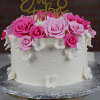 The BR-000G is a white cake with pink and white fondant roses, small white flowers, and a gold "Bride to Be" diamond ring topper, displayed on a cake stand.
