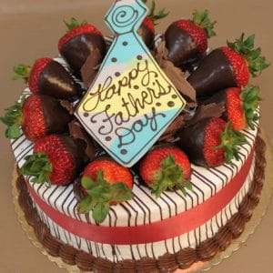 The FD-003 Strawberry Grand Marnier is a round cake topped with chocolate-dipped strawberries, chocolate shavings, a red ribbon, and a tie-shaped cookie that says "Happy Fathers Day.