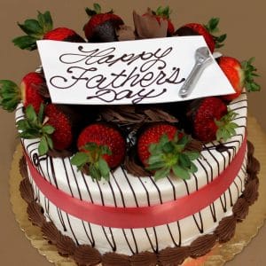 FD-007 is a round cake adorned with chocolate-dipped strawberries, chocolate shavings, a red ribbon, a “Happy Fathers Day” cursive sign on top, and finished with a small decorative razor.