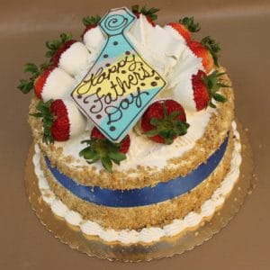 FD-008 Carrot cake: A round carrot cake adorned with fresh strawberries, whipped cream, a blue ribbon, and a tie-shaped cookie reading "Happy Fathers Day," all presented on a gold cake board.