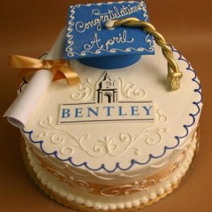 The GC-042A Bentley is a round graduation cake with blue and gold icing, Bentley University’s logo, a blue cap and gold tassel, a diploma, and “Congratulations April” written on top.