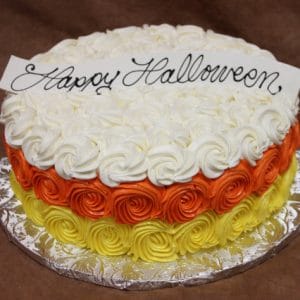 The HW-005 is a round cake adorned with rows of yellow, orange, and white icing roses, finished with a white plaque reading "Happy Halloween" in cursive. It is presented on a decorative silver board.