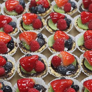 CO-070 Fruit Tarts arranged on a tray, each in a white paper cup and topped with strawberries, raspberries, blueberries, and kiwi slices.