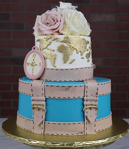 The BR-000B is a two-tiered cake featuring a blue and beige suitcase base, world map and compass on the top tier, pink and white roses on top, displayed on a gold base with a brick wall background.