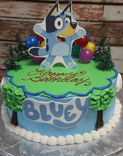 The SC-080 Bluey cake is a round birthday cake with tree and balloon decorations, a big edible Bluey cartoon topper, "Happy Birthday" in red icing, and "BLUEY" in blue letters on the side.