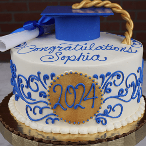 The GC-017 is a round graduation cake featuring “Congratulations Sophia” in blue icing, a gold “2024” plaque, blue and gold decorations, a blue grad cap with gold tassel, and a diploma on top.