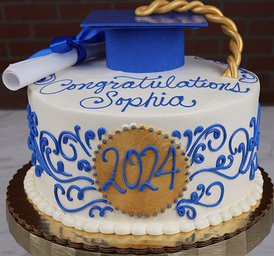 The GC-017 is a round graduation cake featuring “Congratulations Sophia” in blue icing, a gold “2024” plaque, blue and gold decorations, a blue grad cap with gold tassel, and a diploma on top.