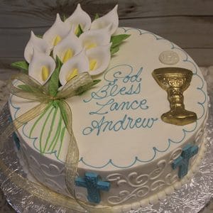 RC-007 is a round white cake featuring calla lilies, gold chalice, blue crosses, and a gold ribbon. Blue piping spells "God Bless Lance Andrew." Presented on a silver platter with a wooden background.