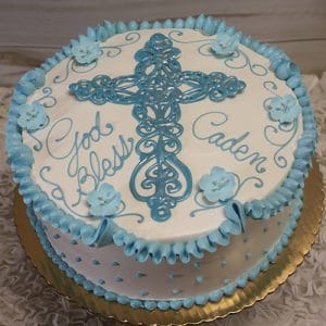 RC-016 is a round white cake with blue icing, a large cross in the center, blue flowers, and "God Bless Caden" in cursive. Presented on a gold board.