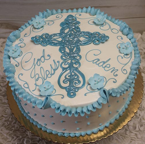 RC-016 is a round white cake with blue icing, a large cross in the center, blue flowers, and "God Bless Caden" in cursive. Presented on a gold board.