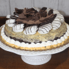 GD-006 Oreo Cheesecake is topped with striped chocolate-dipped cookies, chocolate shavings, and whipped cream, and is displayed on a white cake stand.