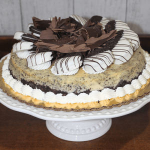 GD-006 Oreo Cheesecake is topped with striped chocolate-dipped cookies, chocolate shavings, and whipped cream, and is displayed on a white cake stand.