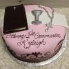 The RC-073 is a pink and white cake featuring a Bible, chalice, rosary, and “Happy 1st Communion Kyleigh” in brown icing. Presented on a silver cake board.