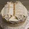 RC-097: A round white cake with gold accents, white roses, and an open book topper featuring a gold cross and "God Bless Martyna" written in gold icing.