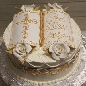 RC-097: A round white cake with gold accents, white roses, and an open book topper featuring a gold cross and "God Bless Martyna" written in gold icing.