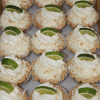 CO-071 Key lime Tarts, each topped with whipped cream, shredded coconut, and a slice of lime, are neatly arranged in rows on a parchment-lined tray.