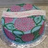 BD-147 is a round blue cake featuring pink and green floral designs, a white banner with "Happy 17th Birthday Julia!" in pink script, and is presented on a silver board.