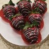 Six VC-031 Chocolate dipped strawberries with pink and white drizzle and heart-shaped sprinkles are arranged on a silver stand, each in a red paper cup.