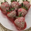 Six VC-033 Milk chocolate dipped strawberries with leafy tops, pink and white drizzle, and heart-shaped sprinkles are arranged on a silver stand with a decorative edge.