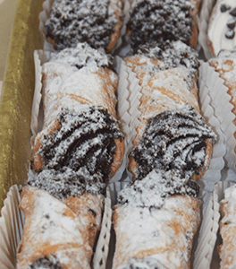 A tray of CO-081 Chocolate filled Cannolis, dusted with powdered sugar and arranged neatly in paper liners.