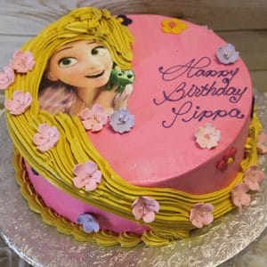 The CB-008G is a round pink birthday cake featuring Rapunzel from Tangled, yellow icing like her hair, pastel flowers, and "Happy Birthday Pippa" written in purple icing.