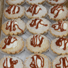 A tray of CO-079 Apple Caramel Cheesecake—small, round tarts topped with powdered sugar, whipped cream, and caramel sauce—arranged neatly on parchment paper.