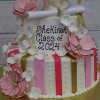 The GC-067 is a two-tiered graduation cake with pink flowers, gold and pink stripes, a diploma, and cap. "Shekinah Class of 2024" is written in black icing.
