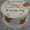The BB-000E is a round white cake featuring orange cartoon tangerines, yellow flowers, and "A little cutie is on the way" written in black and orange icing.