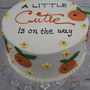 The BB-000E is a round white cake featuring orange cartoon tangerines, yellow flowers, and "A little cutie is on the way" written in black and orange icing.