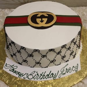 A round "BD-031 Designer Belt" cake with a gold logo, red and green stripe, black repeating patterns, and a front card saying “Happy Birthday Greg” in green script.
