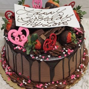 The VC-008 cake features chocolate-dipped strawberries, pink and red heart shapes, chocolate drizzle, and "Happy Birthday My Love" written in elegant script on a white card. Pink and white heart sprinkles surround the cake.