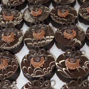 Rows of CO-024 3" Chocolate Decadence Gluten Free desserts with glossy tops, white and dark chocolate swirls, piped chocolate cream, and decorative chocolate loops neatly arranged on a tray.