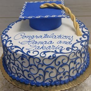 A round GC-030 graduation cake with blue and white icing, blue scrollwork, and a blue fondant cap. “Congratulations Hanaa and Zakaria” is written in blue script on top.