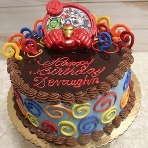 A chocolate-frosted birthday cake, decorated with colorful swirls, an Iron Man topper, and a round Avengers image. "Happy Birthday Devaughn" is written in red icing on top. Product Name: SC-057 Avengers.