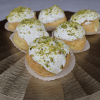 Pistachio Cream Puffs topped with white icing and crushed pistachios, arranged on a gold, striped platter.