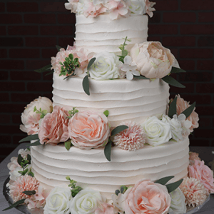 The WD-001U is a three-tier white cake with textured icing, decorated with pink and white roses and peonies, displayed on a silver platter against a dark brick background.